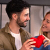casal heterossexual se olhando sorrindo e segurando um coração vermelho