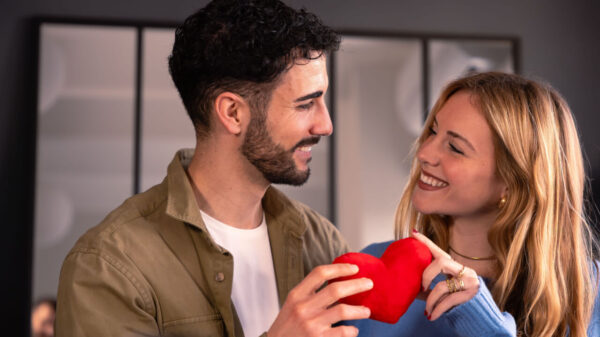 casal heterossexual se olhando sorrindo e segurando um coração vermelho