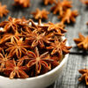 à esquerda está um pote branco cheio de anis-estrelado e os restante da mesa esta preenchido com anis-estrelado em cima de uma mesa da madeira