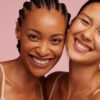duas mulheres se abraçando e sorrindo em fundo rosa