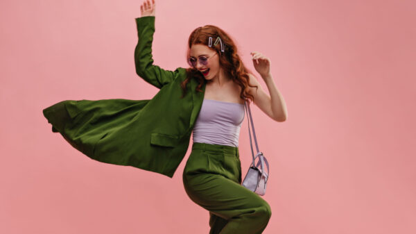 mulher com roupa verde em em posição de comemoração em fundo rosa