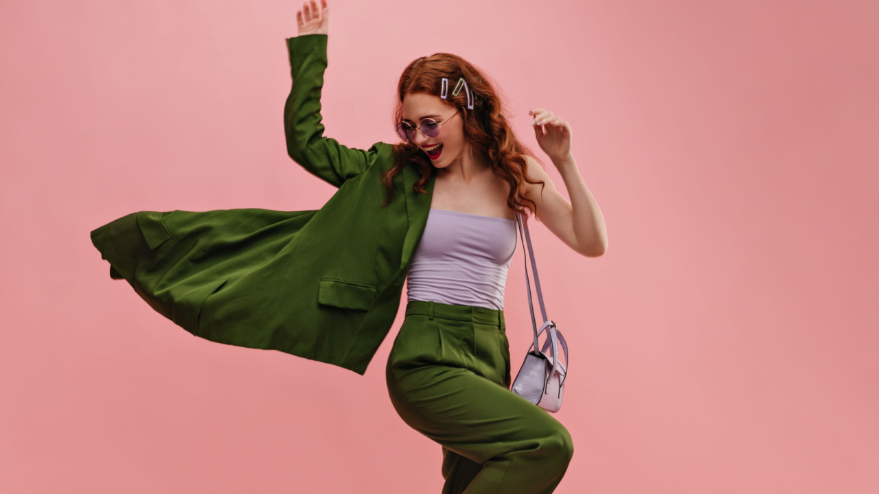 mulher com roupa verde em em posição de comemoração em fundo rosa