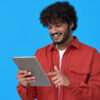 Homem feliz, sorrindo, usando um tablet, isolado em um fundo azul.