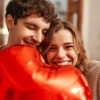 casal heterossexual juntos sorrindo e segurando um balão de coração na altura da boca