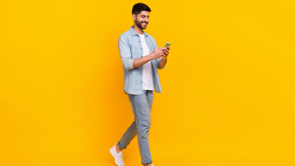 homem em pé mexendo no celular em fundo azul