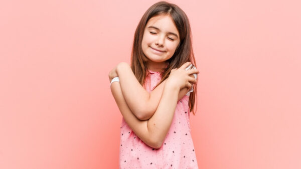Menina se abraçando, sorrindo, despreocupada e feliz.