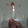 par de mãos segurando uma vela branca em uma sala também branca