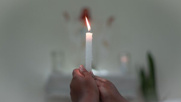 par de mãos segurando uma vela branca em uma sala também branca