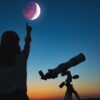 fotografia de uma menina ao lado de um telescópio e apontando para um eclipse lunar
