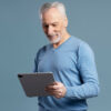 Homem sorrindo, segurando um tablet, isolado em um fundo azul.