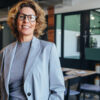 fotografia de uma mulher em primeiro plano vestindo social e sorrindo em um fundo desfocado de um escritório