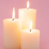 três velas grossas acessas em um fundo rosa