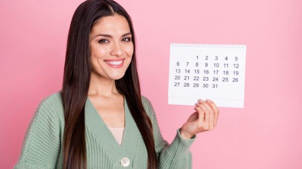 mulher sorrindo e segurando um calendário em fundo rosa