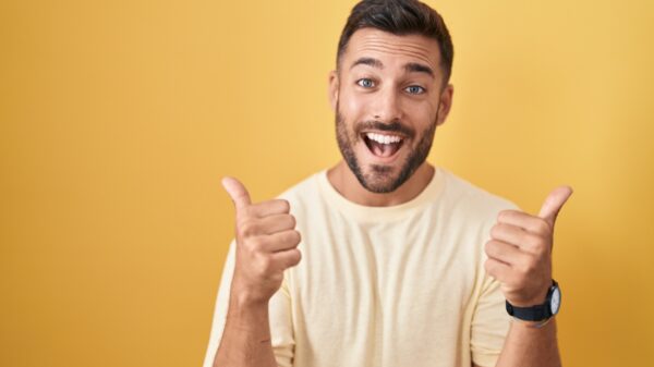 homem fazendo o sinal de positivo com as duas mãos e sorrindo em fundo amarelo