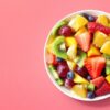 tigela branca fotografada de cima recheada de frutas em fundo rosa