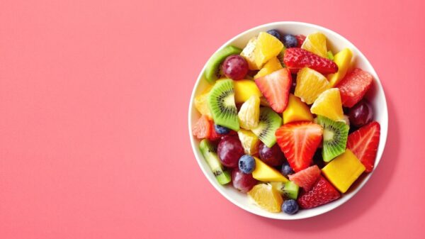 tigela branca fotografada de cima recheada de frutas em fundo rosa