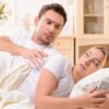 casal deitado na cama com ele tentando olhar o que está no celular dela