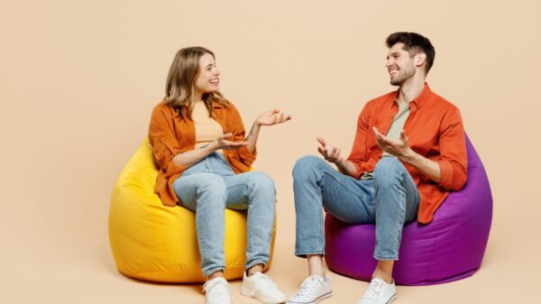 casal conversando cada um sentado em um puff em fundo bege