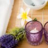 à esquerda tá parte de uma banheira branca e quadrada cheia de espumas e à direta há velas lavandas e margaridas em cima de uma mesa de madeira