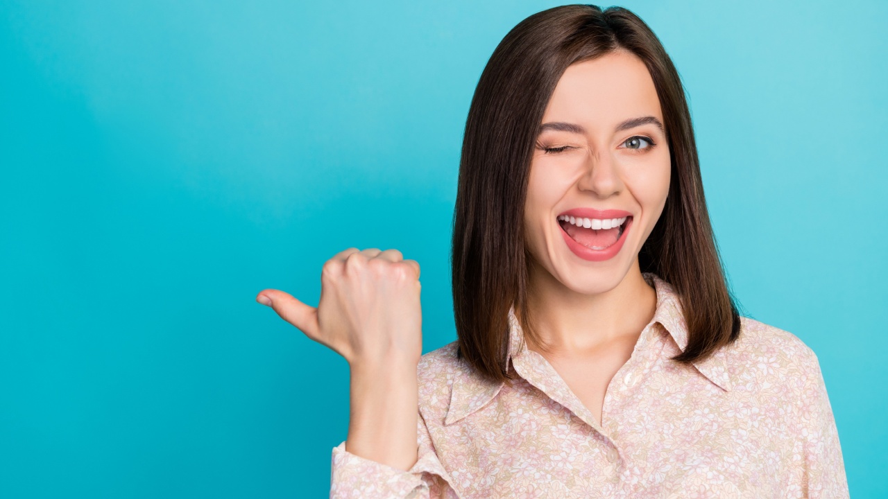 mulher sorrindo e piscando um olho e apontando o lado para o lado esquerdo em fundo azul