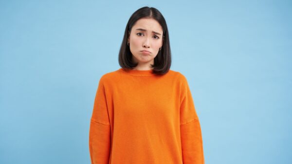 mulher ao centro com cara chateada vestindo moletom laranja em fundo azul claro