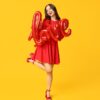 no centro da imagem há uma mulher com vestido vermelho e segurando um balão vermelho que forma a palavra love em fundo amarelo