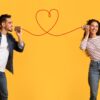 casal heterossexual em fundo amarelo. cada um segura uma lata e a linha vermelha que une elas forma um coração