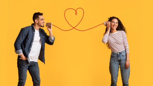 casal heterossexual em fundo amarelo. cada um segura uma lata e a linha vermelha que une elas forma um coração