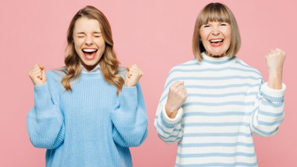 mãe e filha, cada uma em um canto da imagem, fazendo gesto de comemoração em fundo rosa
