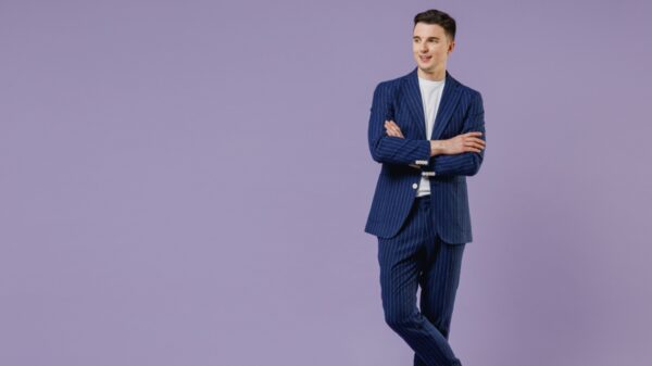 No canto direito há um homem branco em pé e usando um terno azul. O resto da imagem é um fundo roxo