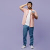 Homem chocado, assustado, usando uma camisa rosa e uma camiseta branca por baixo, roupas casuais, segurando um celular, com a mão na cabeça, isolado em um estúdio de fundo roxo pastel simples.