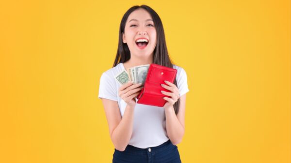 mulher com traços asiáticos segurando uma carteira vermelha e tirando dinheiro dela em fundo amarelo