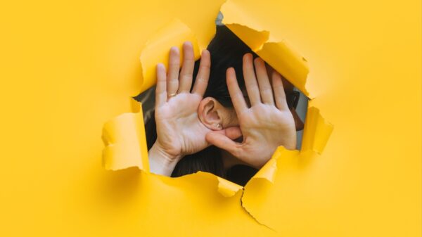 mulher ouvido através de uma parede amarelo com buraco no meio