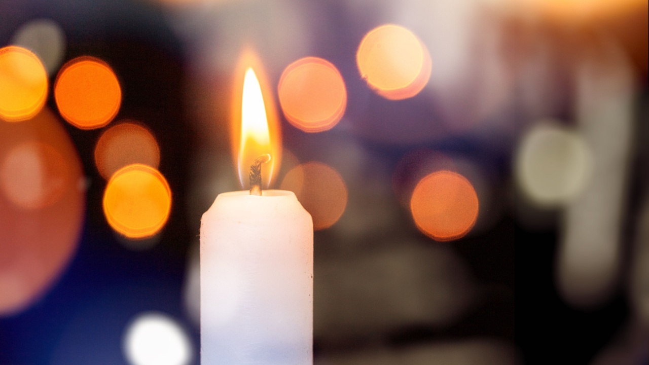 imagem de uma vela branca acesa com o fundo desfocado e pontos de luz