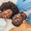 casal deitados no chão, encima de um tapete. se olhando e sorrindo