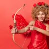 mulher vestida de cupido com três corações na cabeça e mirando o arco e flecha