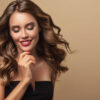 Mulher sorrindo, com cabelos longos e ondulados, e unhas vermelhas. Conceito de beleza e maquiagem.