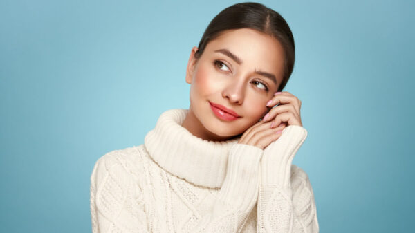 Retrato de uma mulher feliz, sorrindo e olhando para o lado, isolada em um fundo azul, usando um suéter branco. Conceito de inverno.