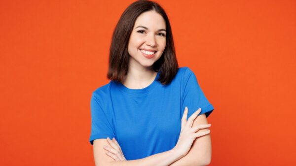 mulher no centro da imagem sorrindo com os os braços cruzados em fundo laranja