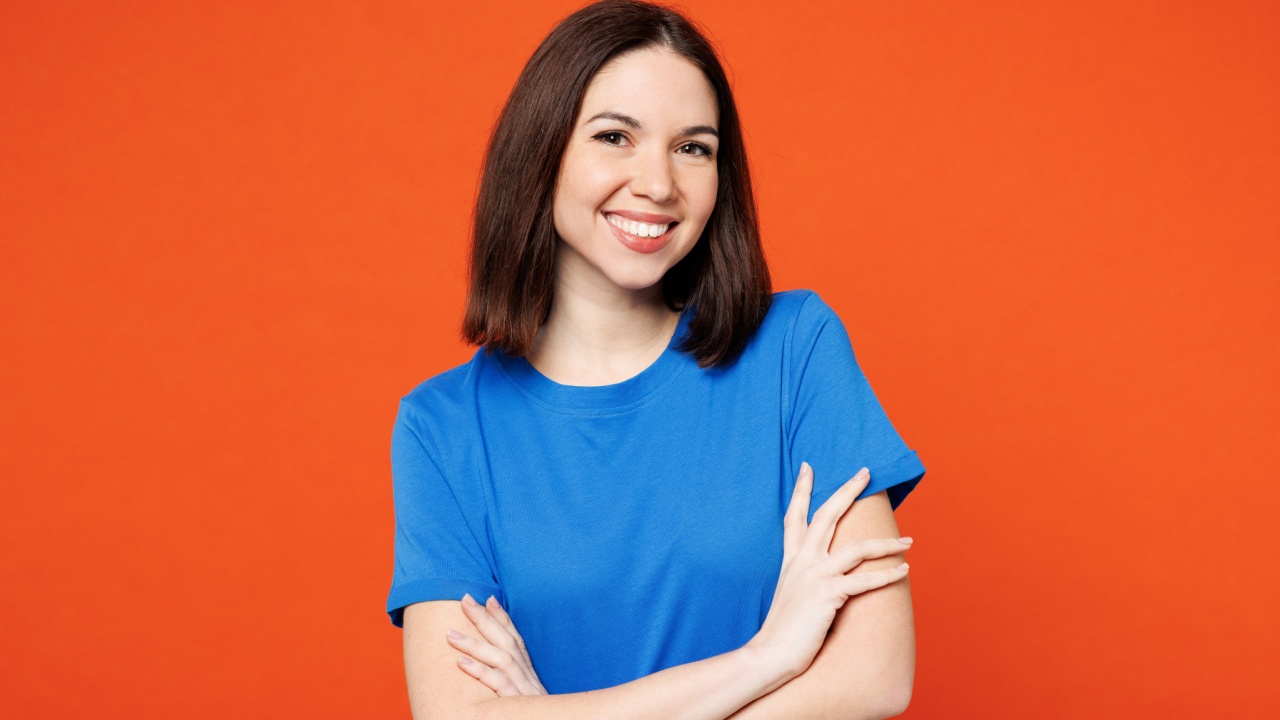 mulher no centro da imagem sorrindo com os os braços cruzados em fundo laranja