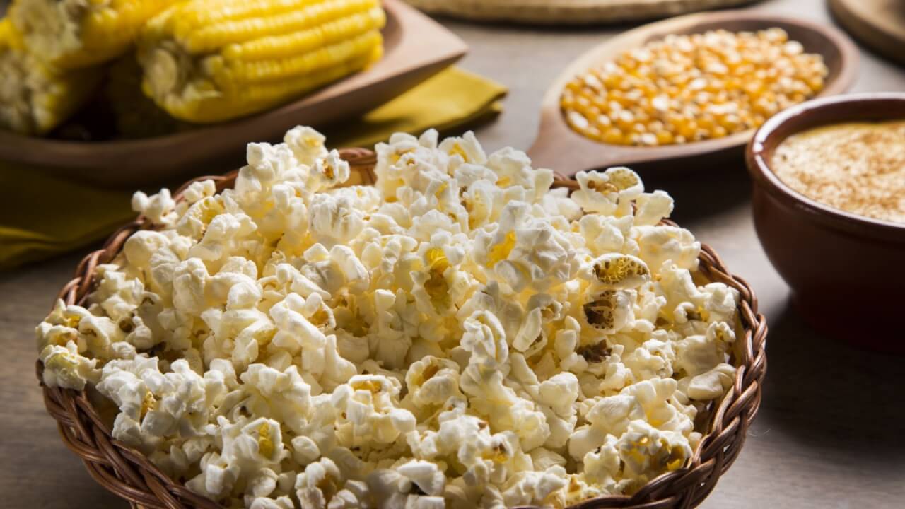 imagem de uma bacia de pipoca com espigas de milho ao fundo