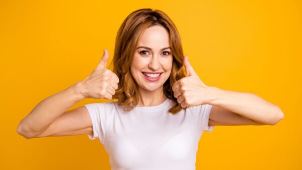 mulher sorrindo e com as duas mãos fazendo joia em fundo amarelo