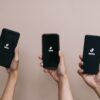 três mãos segurando cada um celular cada um com o aplicativo tiktok aperto em fundo rosinha