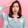 mulher com a mão na cabeça e expressão facial de assustada em fundo rosa