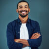 Retrato de um homem de braços cruzados, feliz, sorrindo e confiante em um estúdio, isolado em um fundo escuro.