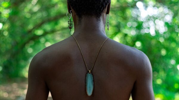 foto de um homem negro de costas em uma mata com objetos da religião africana