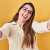 mulher usando roupa branca sorrindo e de braços abertos em fundo amarelo