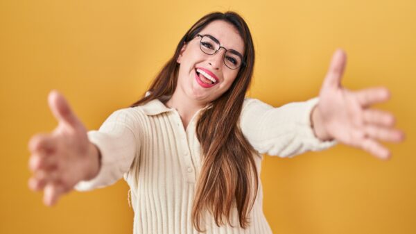 mulher usando roupa branca sorrindo e de braços abertos em fundo amarelo