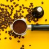 grãos de café sendo moidos para virar pó em uma fundo amarelo