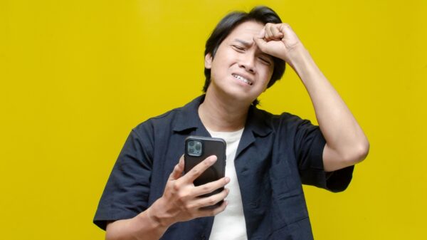 homem com a mão na testa decepcionado e com um celular na mão em fundo amarelo